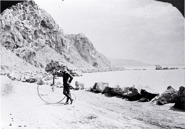 Cyclist beside a penny-farthing bicycle near Shag Rock on the Sumner road, Christchurch Cyclist beside a penny-farthing bicycle near Shag Rock on the Sumner road, Christchurch