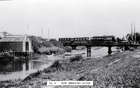 An electric tram crosses the New Brighton bridge with a barge moored underneath
