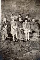 Mixed group some in uniform on banks of river next to fence