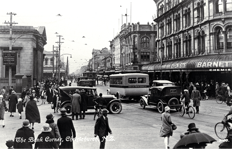 Cars, bicycles and a bus create a busy scene at the Bank corner, Christchurch : Barnett & Co. Chemists in the foreground. Cars, bicycles and a bus create a busy scene at the Bank corner, Christchurch : Barnett & Co. Chemists in the foreground.